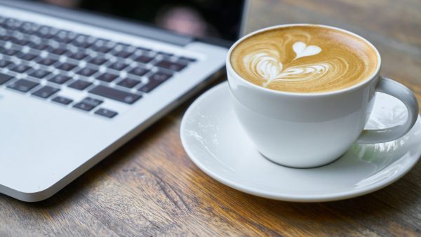 sobre una mesa de madera un ordenador y un café con espuma